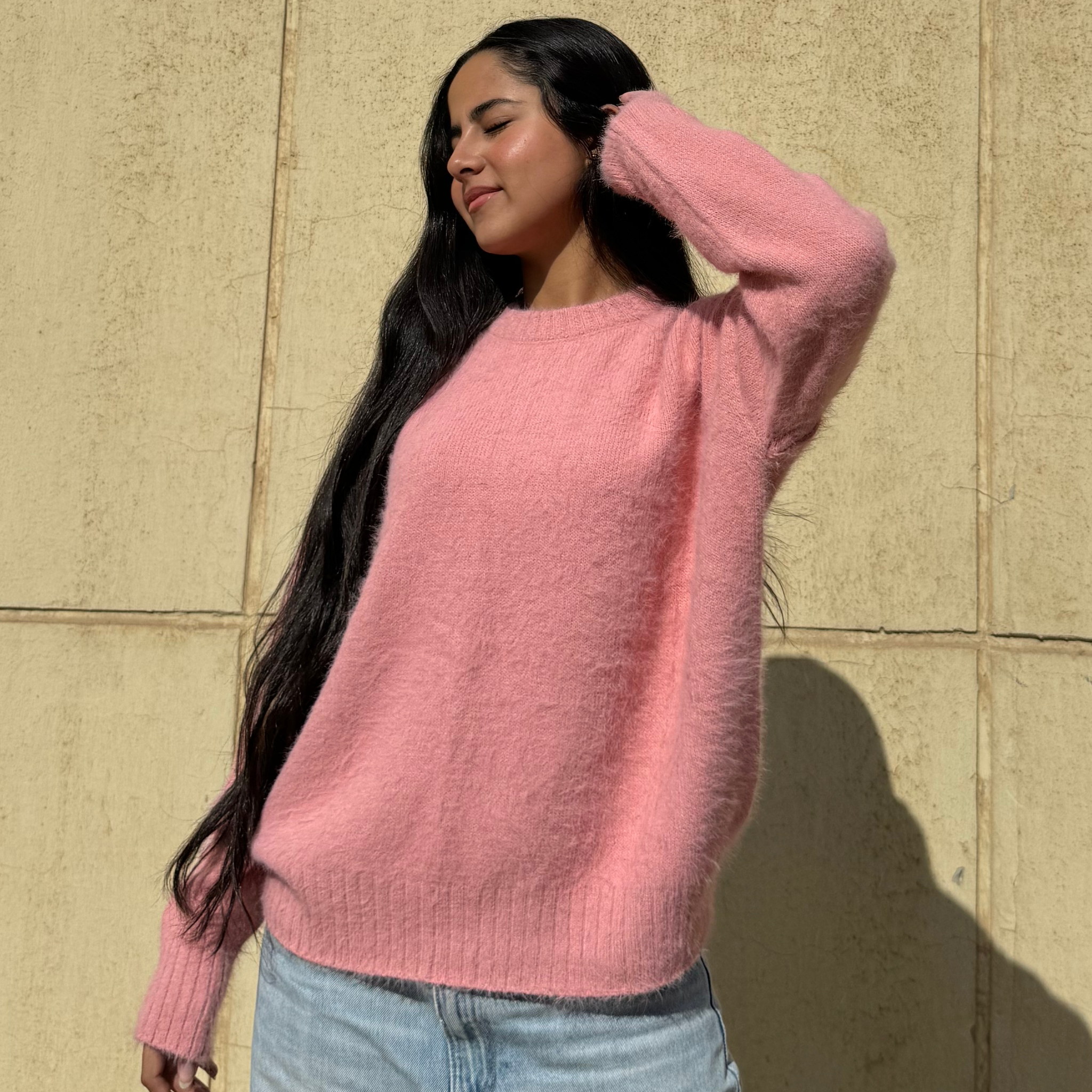 Woman wearing a pink sweater standing against a beige wall