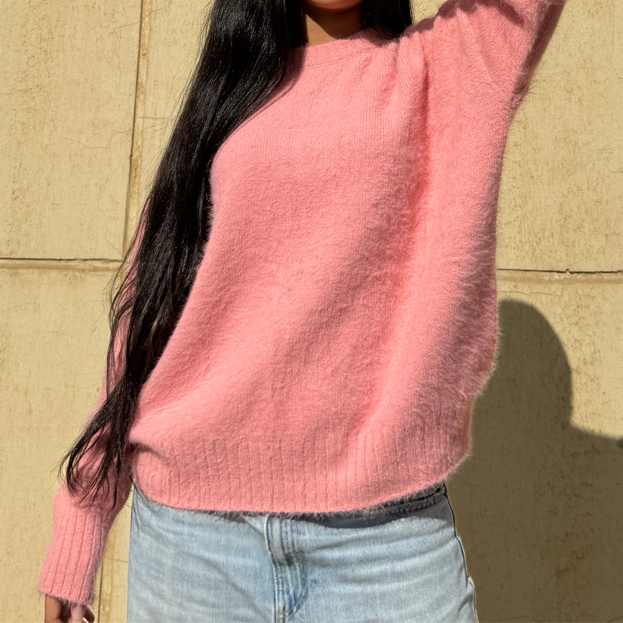 Woman wearing a pink sweater standing against a beige wall
