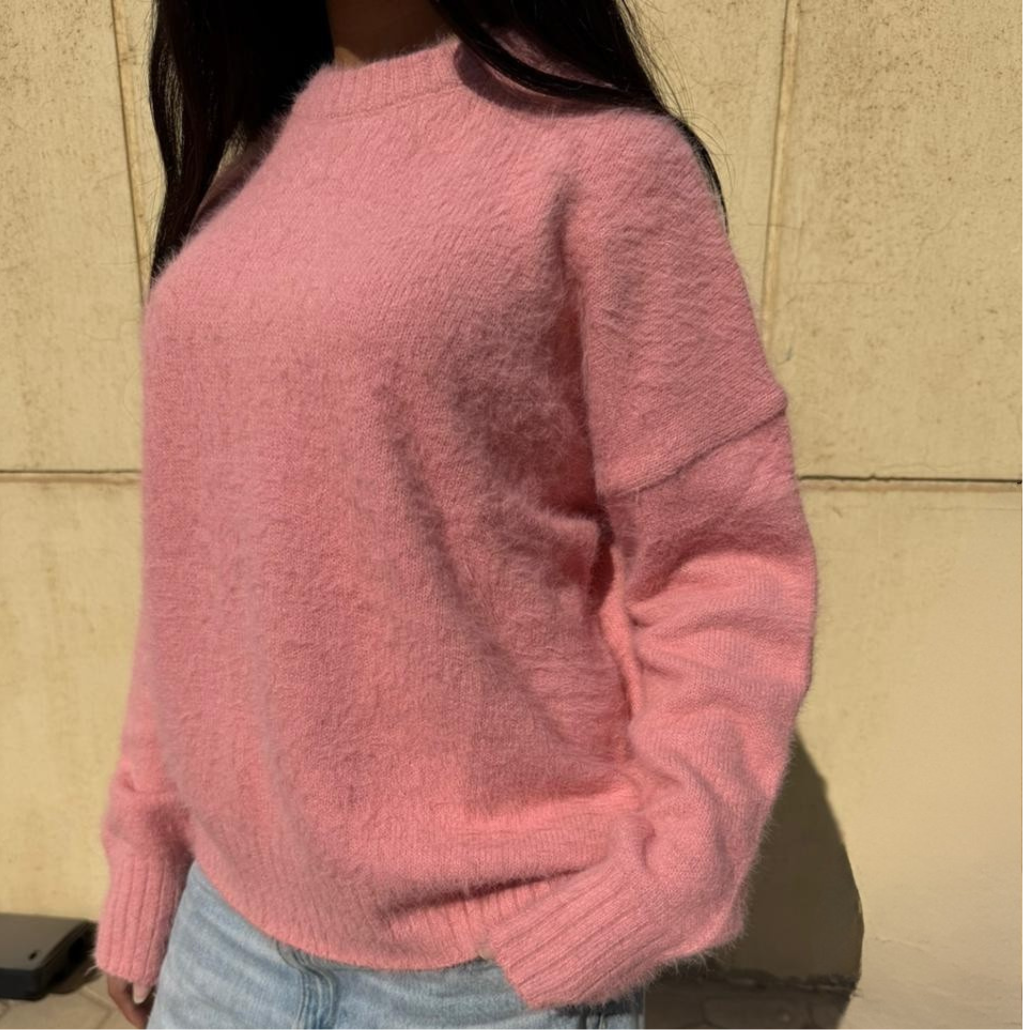 Woman wearing a pink sweater standing against a beige wall