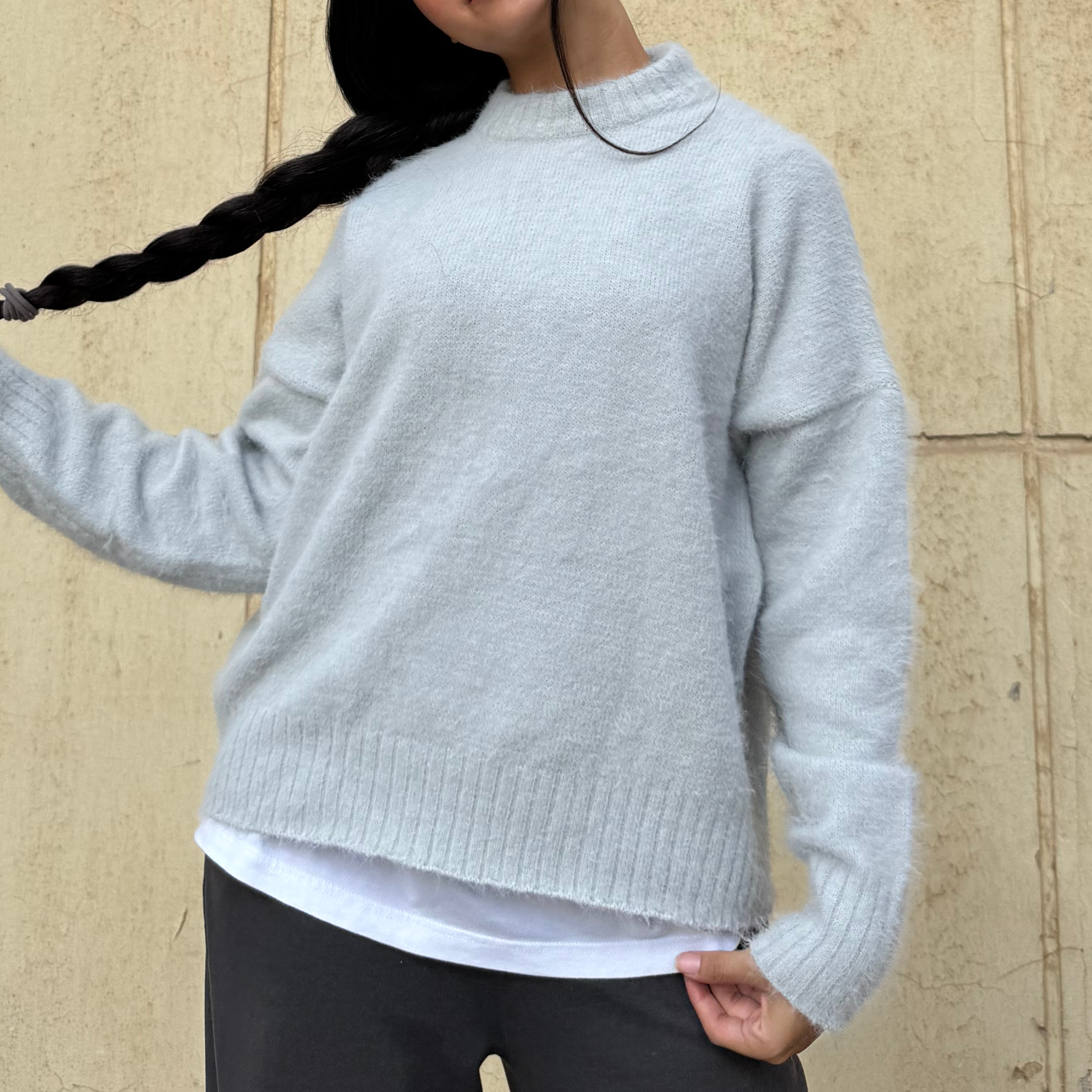 Woman wearing a light gray sweater against a beige wall