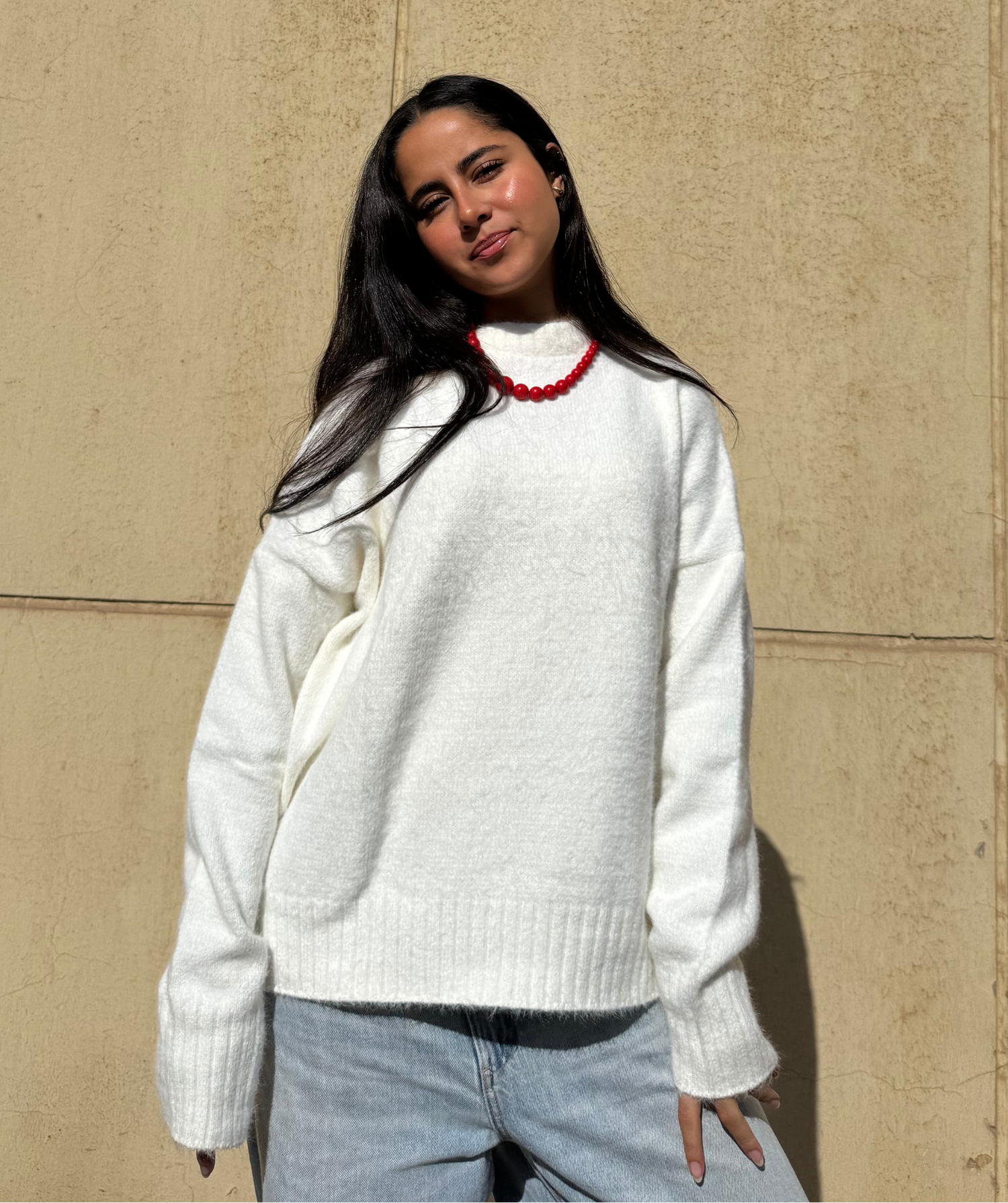 Woman wearing a white sweater  against a beige wall
