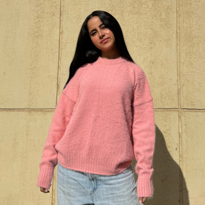 Woman wearing a pink sweater standing against a beige wall
