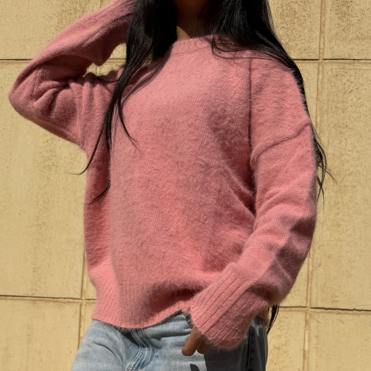 Woman wearing a pink sweater standing against a beige wall