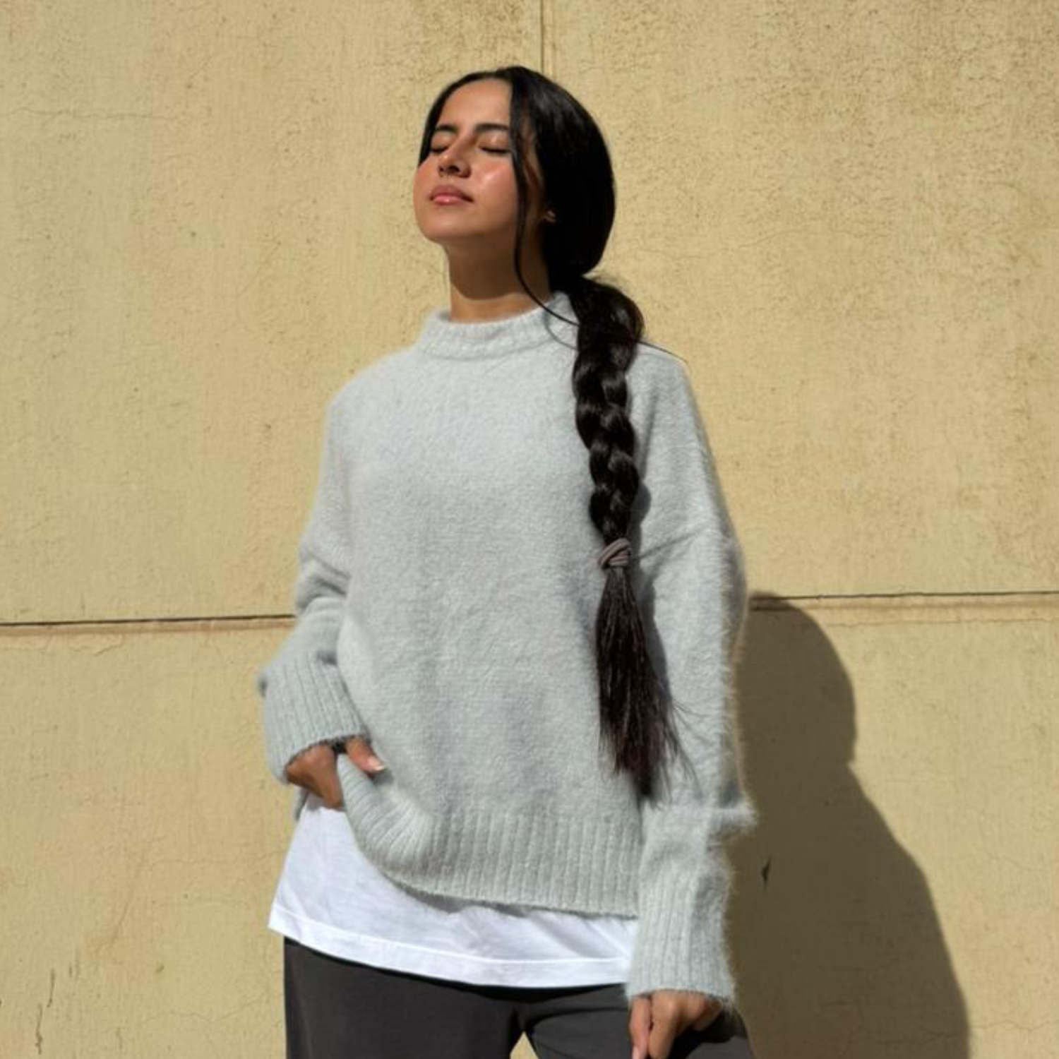 Woman wearing a light gray sweater against a beige wall