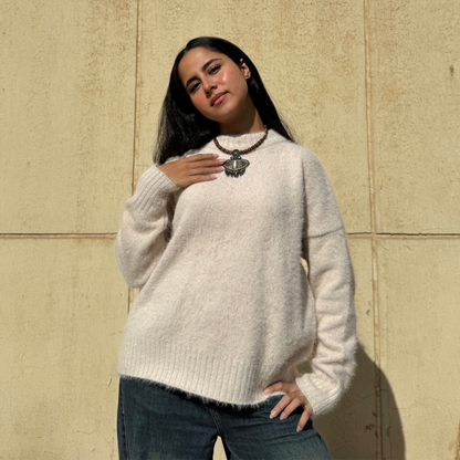 Woman wearing a beige sweater and blue jeans against a beige wall