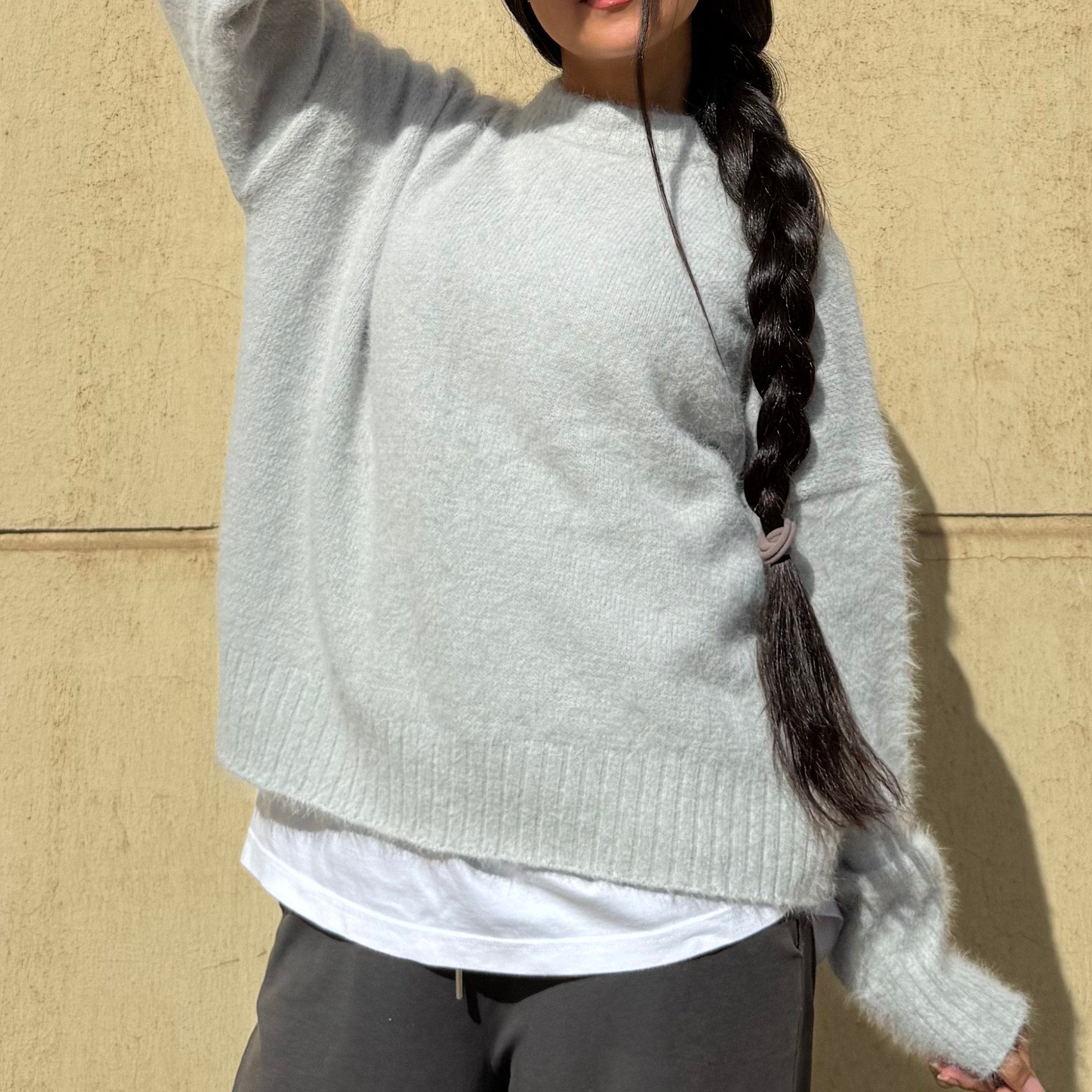 Woman wearing a light gray sweater against a beige wall