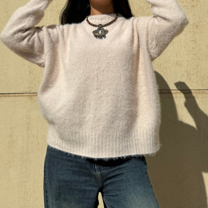 Woman wearing a beige sweater and blue jeans against a beige wall