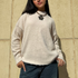 Person wearing a beige sweater and dark jeans against a beige wall