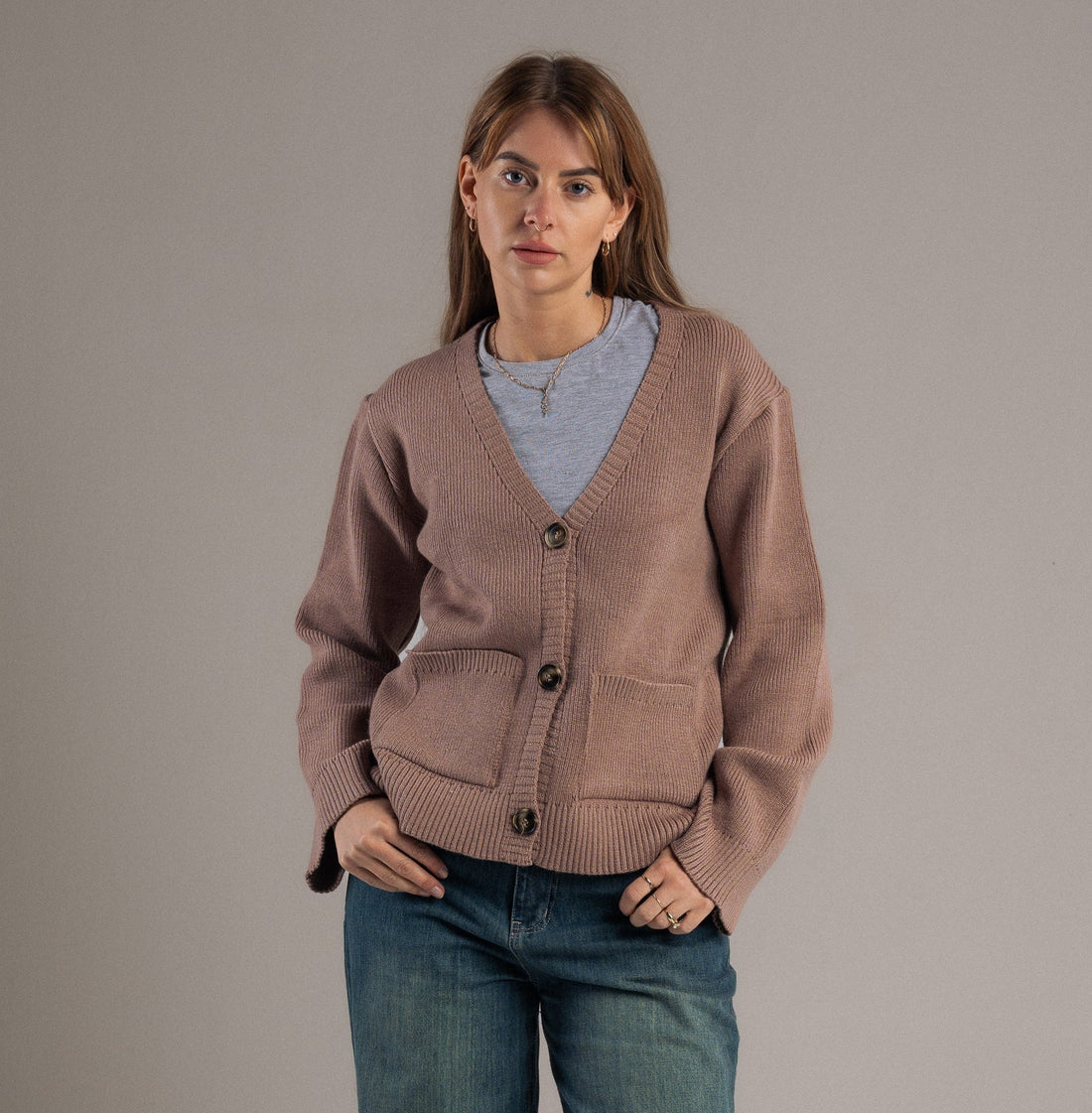 Person wearing a brown cardigan and blue jeans on a plain background